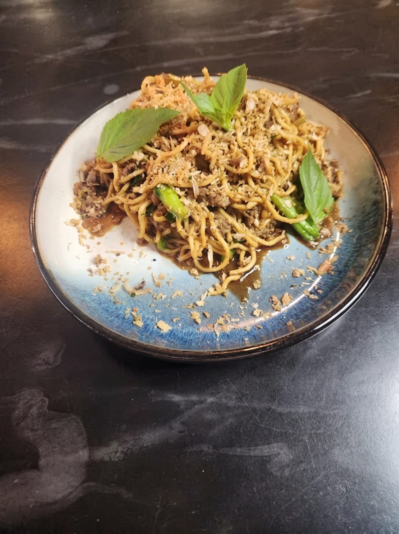 Noodles with ground meat, green beans, and basil on a blue and white plate.